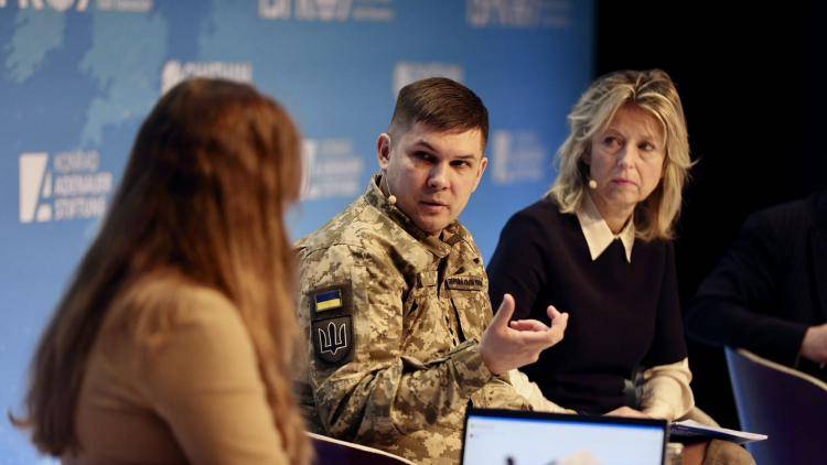 a man in military uniform speaks on stage with two women