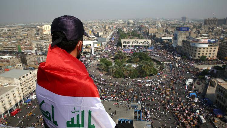 young man wrapped in Iraqi flag looks down towards protestors