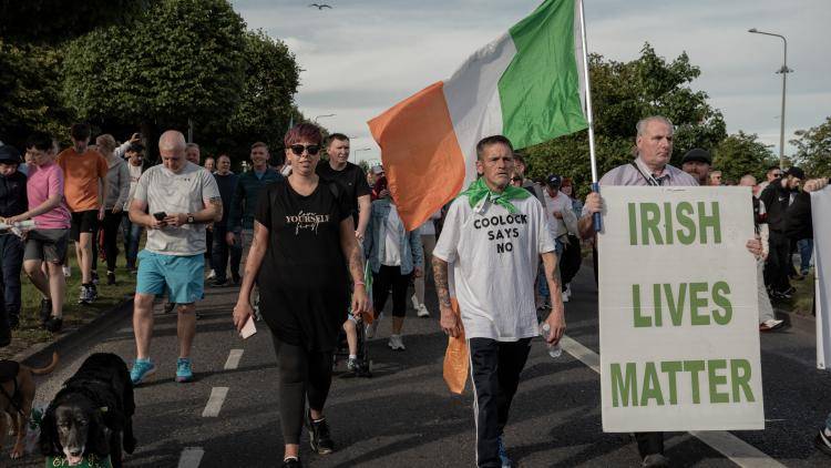 people walk in a protest holding an Irish flag