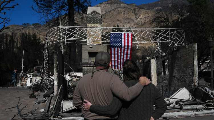 Residents look at their burned Altadena home, where a US flag is draped on the debris.