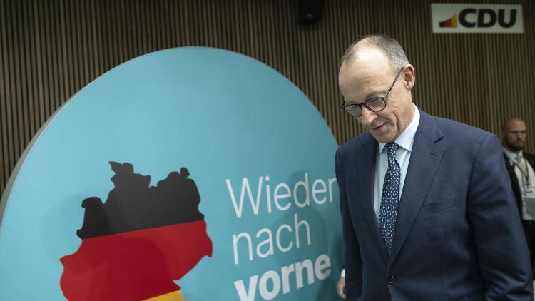 Friedrich Merz, chancellor candidate of Germany’s Christian Democrats arriving for a press conference in front of a slogan and a map of Germany in the black, red and yellow flag colours.