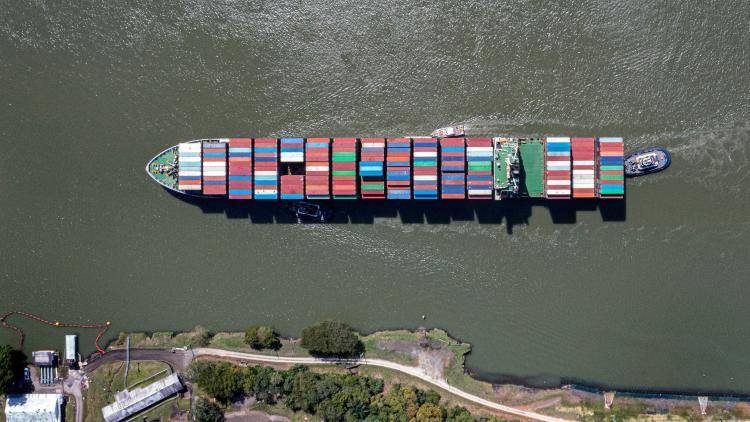Aerial view of a container ship traversing the Panama canal, its deck filled with multi-coloured containers