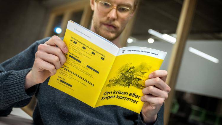 man in dark shirt reads yellow booklet