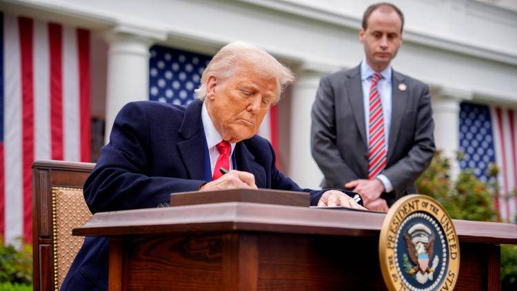 President Donald Trump, accompanied by White House staff secretary Will Scharf, signs executive orders imposing tariffs on imported goods during a 'Make America Wealthy Again' trade announcement event in the Rose Garden at the White House. 