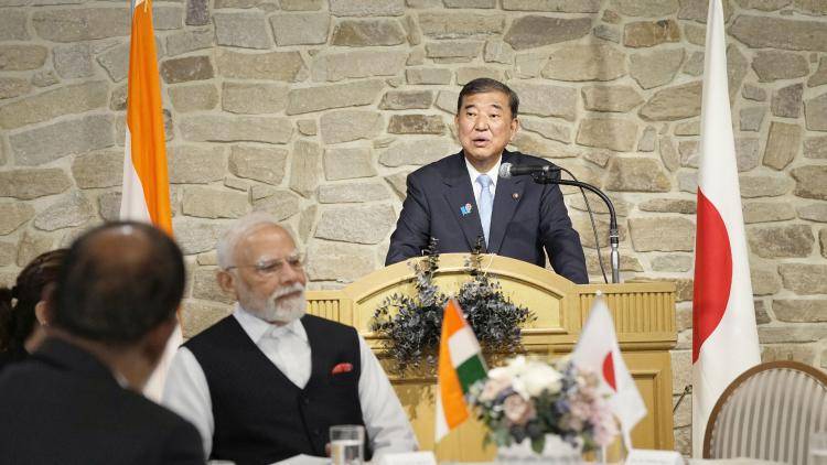 Shigeru Ishiba gives a speech flanked by Indian and Japanese flags, with Prime Minister Modi in the foreground, listening.