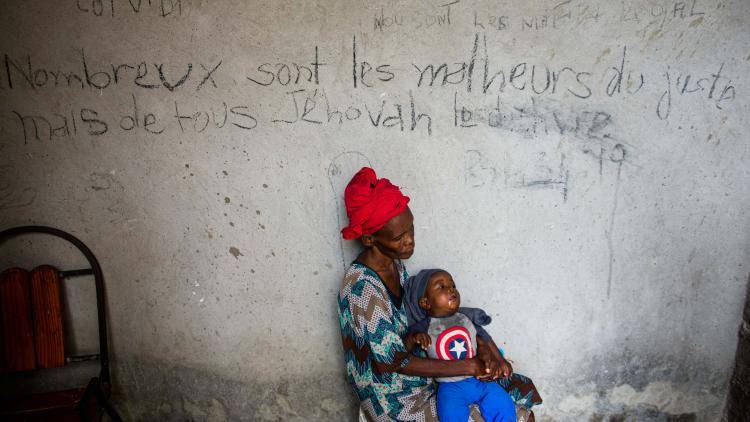 woman holding a young child sits next to wall