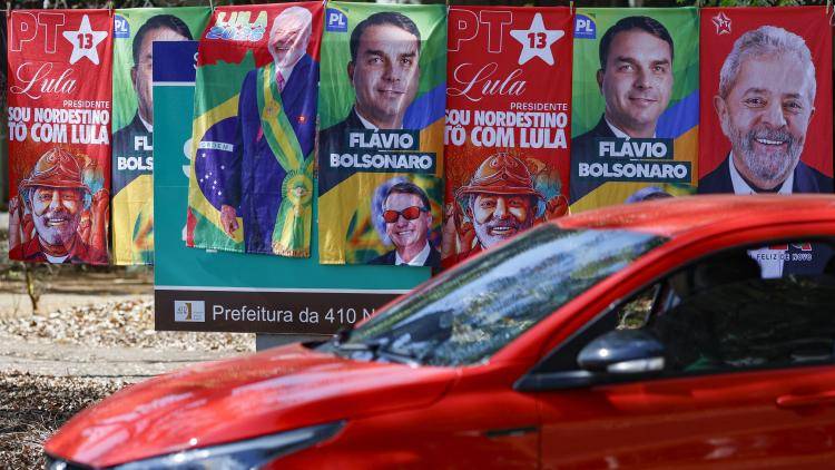 A car drives by a colourful display of election posters featuring presidential candidates Lula and Flavio Bolsonaro in Brasília. 