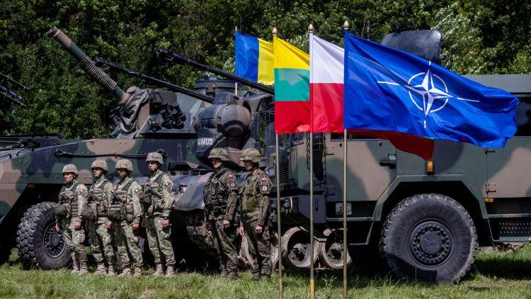 Polish and Romanian soldiers stand next to military vehicles and a Polish and NATO flag.