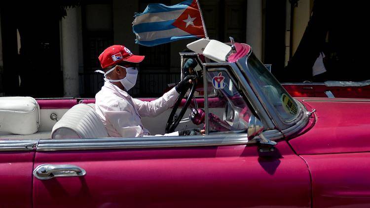 A taxi driver wears a face mask while driving tourists around Havana on 19 March 2020. Photo: Getty Images.