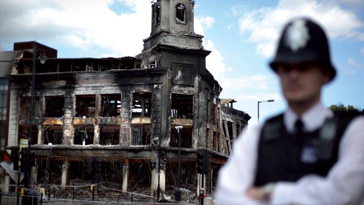 A police officer stands outside the burnt out shell of the Carpetright store in Tottenham. Photo: Peter MacDiarmid/Getty Images