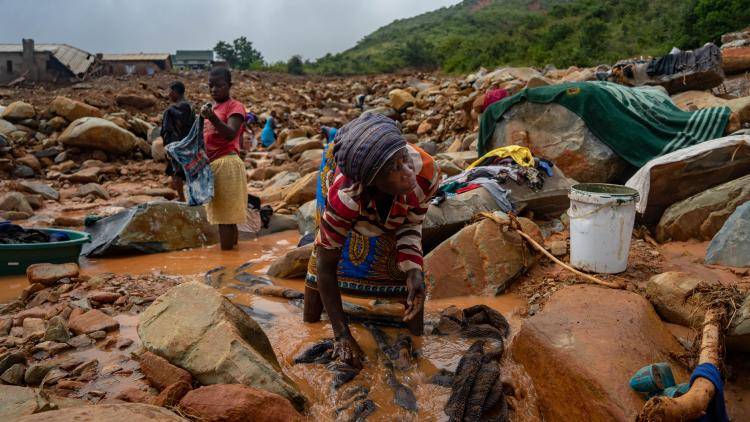 A woman tries to wash her belongings in the mud left after Cyclone Idai left her homeless