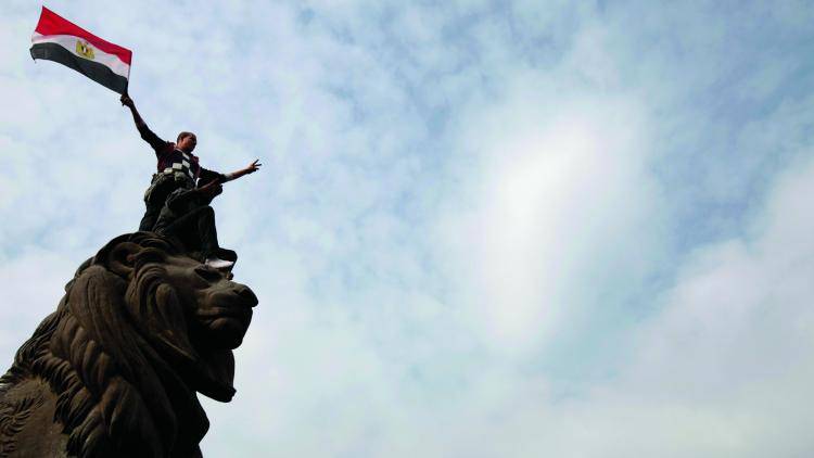 An Egyptian man waves his national flag atop a sculpture in Cairo, Egypt.
