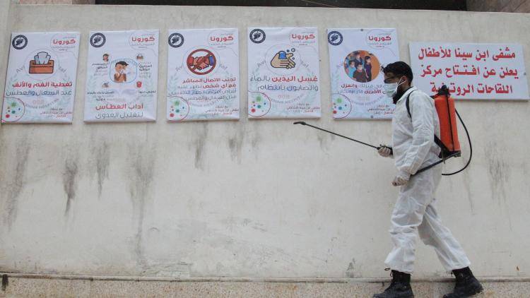 A member of the Syrian Violet NGO disinfects the entrance of Ibn Sina Hospital in Idlib, Syria
