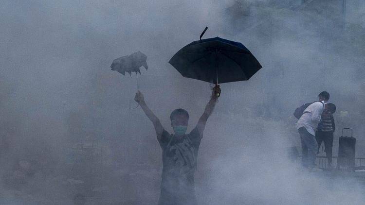 A pro-democracy demonstrator carries an umbrella to fend off clouds of tear gas