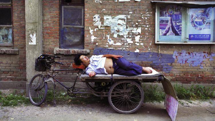 A man sleeps on a three wheeled bicycle in the Jiuxianqiao District in Beijing, China