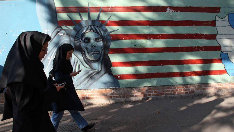 Iranian women walk past an anti-US mural on the wall of the former US embassy in Tehran 