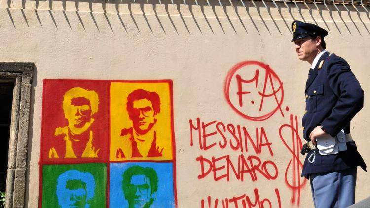 An Italian Police officer in Palermo, Sicily, stands by graffiti portraying Matteo Messina Denaro, a fugitive Mafia boss. 