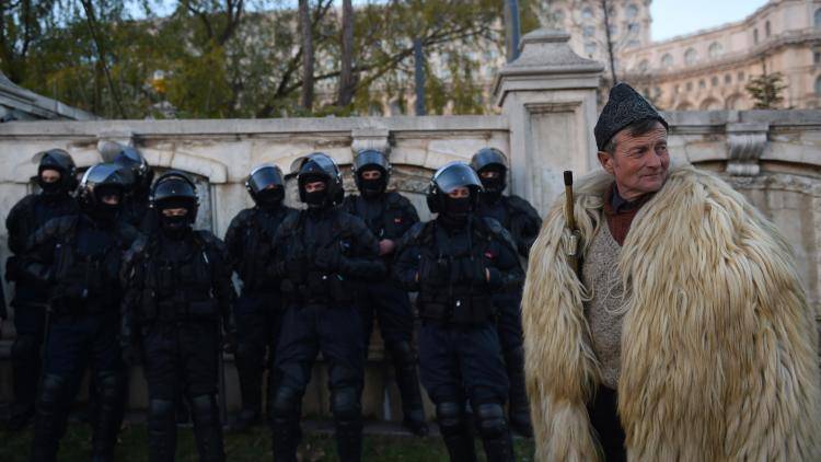 A Romanian shepherd stands next to riot police outside the Parliament building in Bucharest during a protest in December