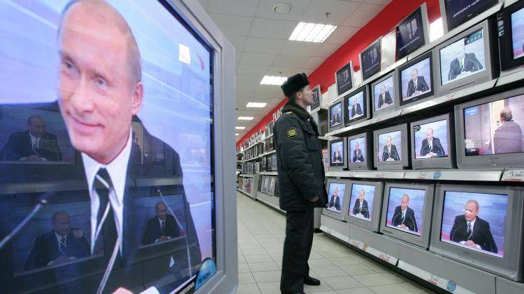 A Russian policeman watches as Putin’s face fills the TV screens in an electronics shop