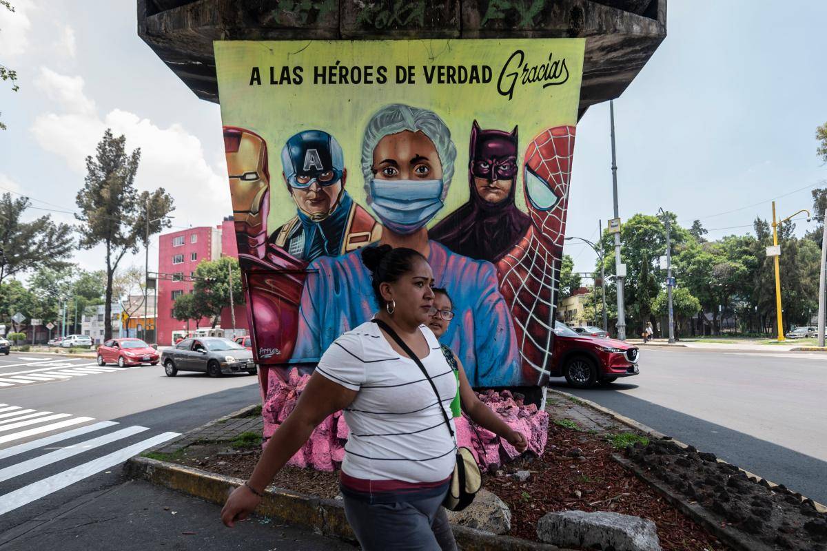 A woman walks past a mural showing a health worker and US superheroes, in Mexico City, on 21 July 2020. Photo credit: Copyright © Pedro Pardo/Getty Images