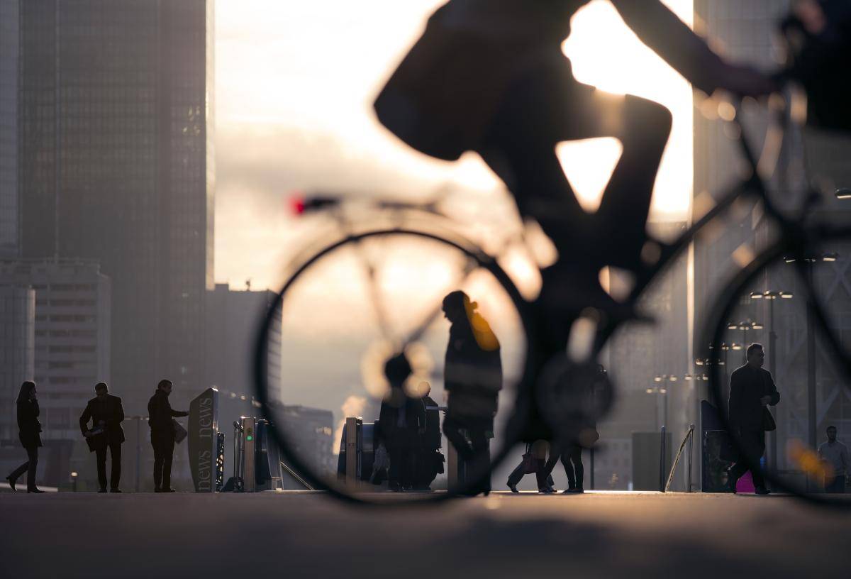 Businessman on bicycle passing skyline of La Défense business district in Paris, France. Photo: EschCollection/Getty Images.