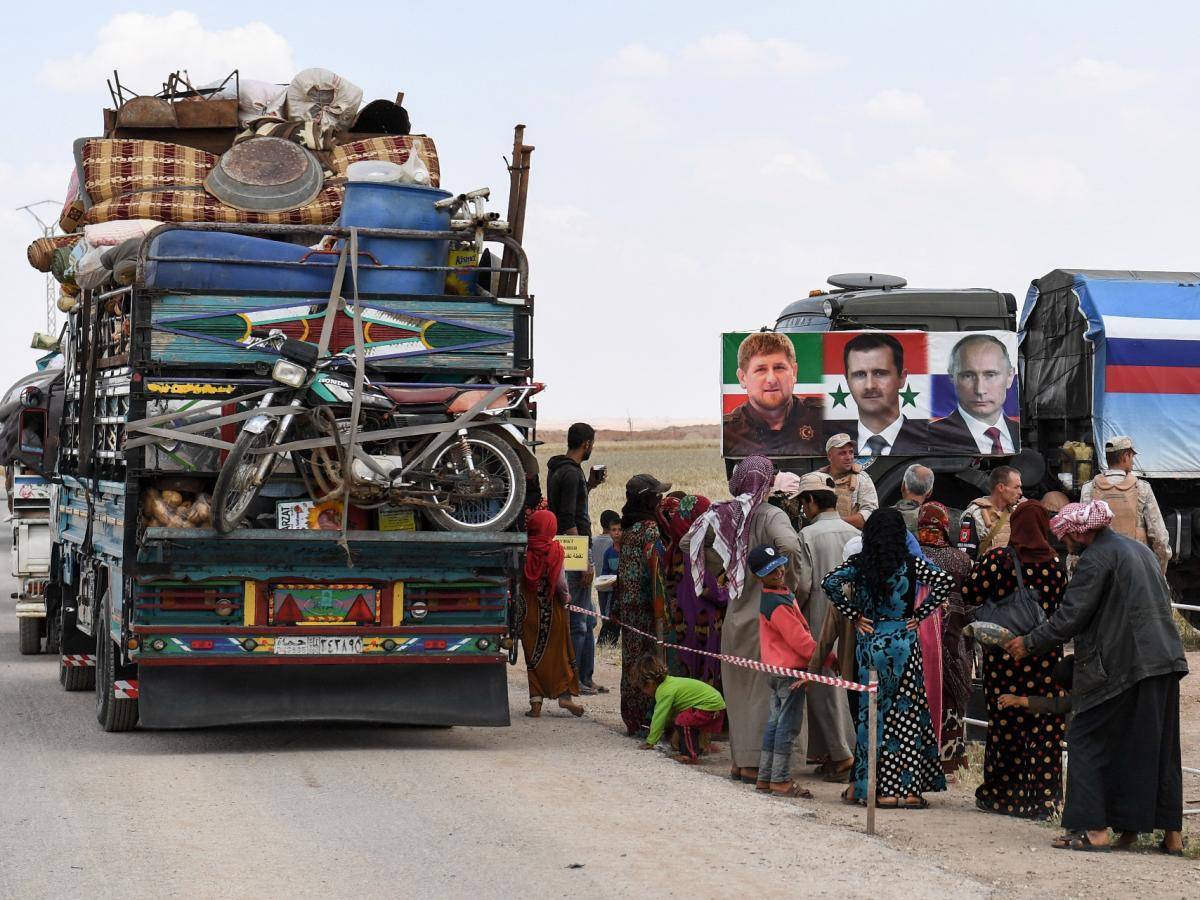 Members of the Russian military police hand out food aid to displaced Syrians returning into government-controlled territory at a checkpoint in Idlib province, 1 June 2018. A banner shows portraits of Chechen leader Ramzan Kadyrov, Syrian President Bashar al-Assad and Russian President Vladimir Putin. Photo: George Ourfalian/AFP/Getty Images