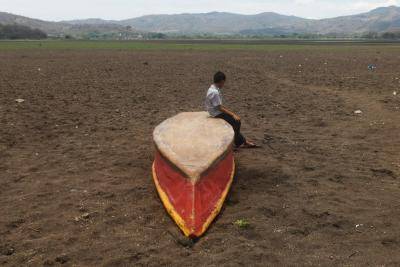 A boy sits on an abandoned boat on what is left of Lake Atescatempa, which has dried up due to drought and high temperatures, in Atescatempa, Guatemala on 5 May 2017.