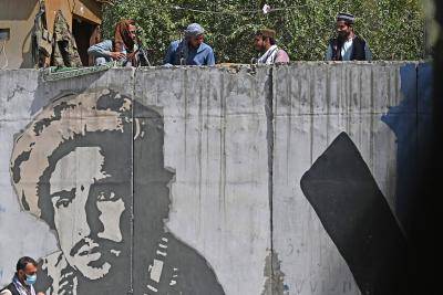 Taliban fighters sit on a concrete barrier wall painted with an image of late Afghan commander Ahmad Shah Massoud as they keep vigil in Kabul on 28 August 2021 following the Taliban's military takeover of Afghanistan.  Photo by AAMIR QURESHI/AFP via Getty Images.