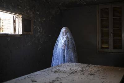 Self-portrait photograph of Egyptian photographer Amina Kadous in a veil holding a bunch of flowers in the dark of her grandmother's old kitchen