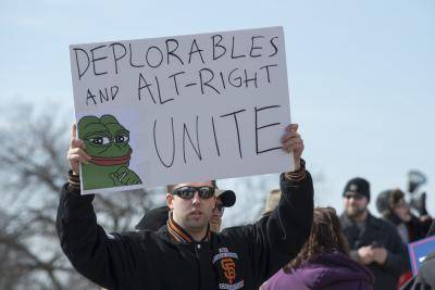 An alt-right demonstrator holds up a sign with Pepe the Frog and the saying 'Deplorables and alt-right unite'