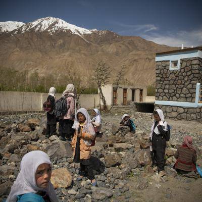 a group of young school girls play in a yard with snow covered mountains behind them. 