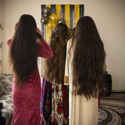 three young girls with long hair stand together with their backs to the camera