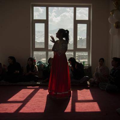 silhouette of a young women in a dress standing in front of a window in a gathering of people 