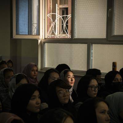 a group of young women in headscarves sit on the floor in dark classroom looking ahead 