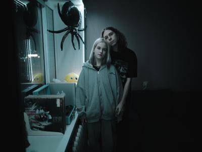 young man and women stand close together in a darkened room facing the camera