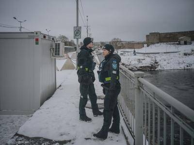two border control officers stand on a snowy bridge over a the river Narva