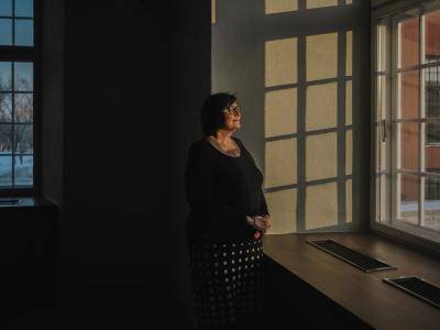 woman stands with her hands clasped together by a window looking out