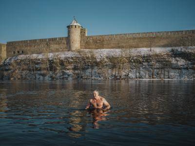 man swims in cold lake in front of stone castle wall