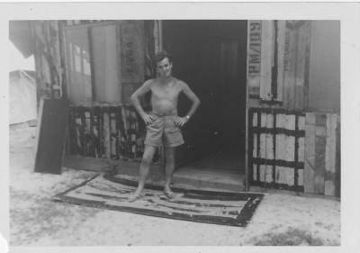 Black and white archive photo of a young man in shorts standing outside structure