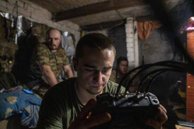 man in military uniform operates a drone from inside a dark shelter