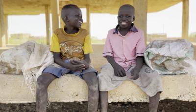 two young boys sit down next to each other on a wall smiling
