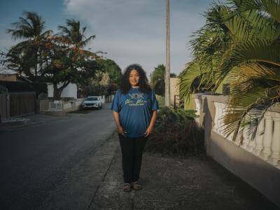 a woman in blue shirt stands on a palm tree lined street 
