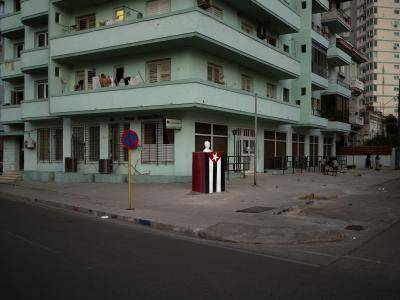 a statue of José Marti stands in front of green building on the streets on Havana