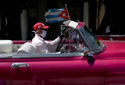 A taxi driver wears a face mask while driving tourists around Havana on 19 March 2020. Photo: Getty Images.