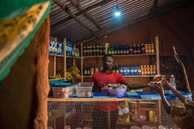 A man serves customers at a shop in Nyahbiheke Refugee Camp, Rwanda. Energy access makes it possible for refugees to power and run businesses. Photo: Practical Action.