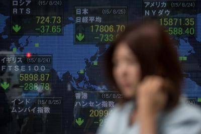 A woman walks past a screen showing global stock market information on the street in Tokyo on 25 August 2015. Photo by Getty Images.