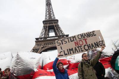 Climate change demonstrators hold up a sign with the text 'system change not climate change' in front of the Eiffel Tower. Photo via Getty Images.