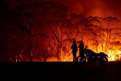 Residents look on as flames burn through bush on 4 January 2020 in Lake Tabourie, NSW. Photo: Getty Images.