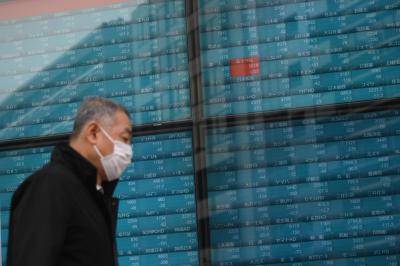 A pedestrian wearing a face mask walks past stock prices in Tokyo on 25 February. Photo: Getty Images.